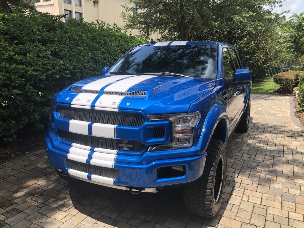 A blue truck with white stripes on the front is parked on a brick driveway.