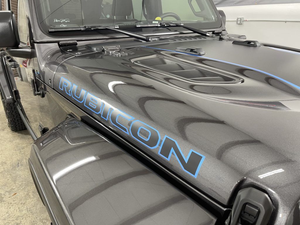 A black jeep with a blue stripe on the hood is parked in a garage.