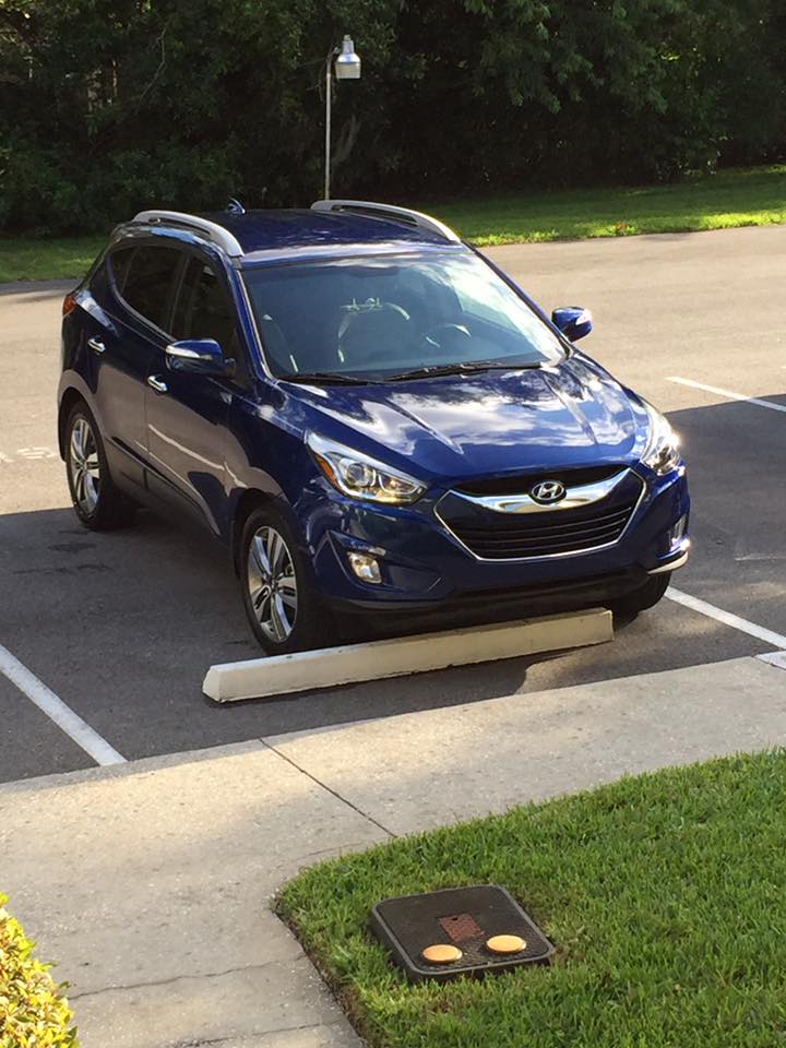 A blue car is parked on the side of the road in a parking lot.