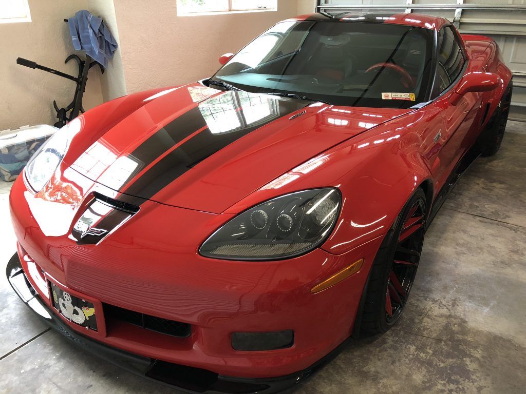 A red sports car with black stripes on the hood is parked in a garage.