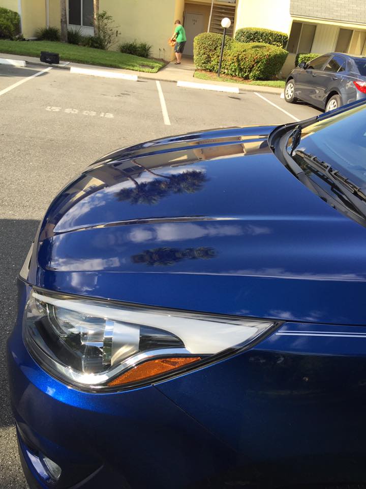 A blue car is parked in a parking lot in front of a building