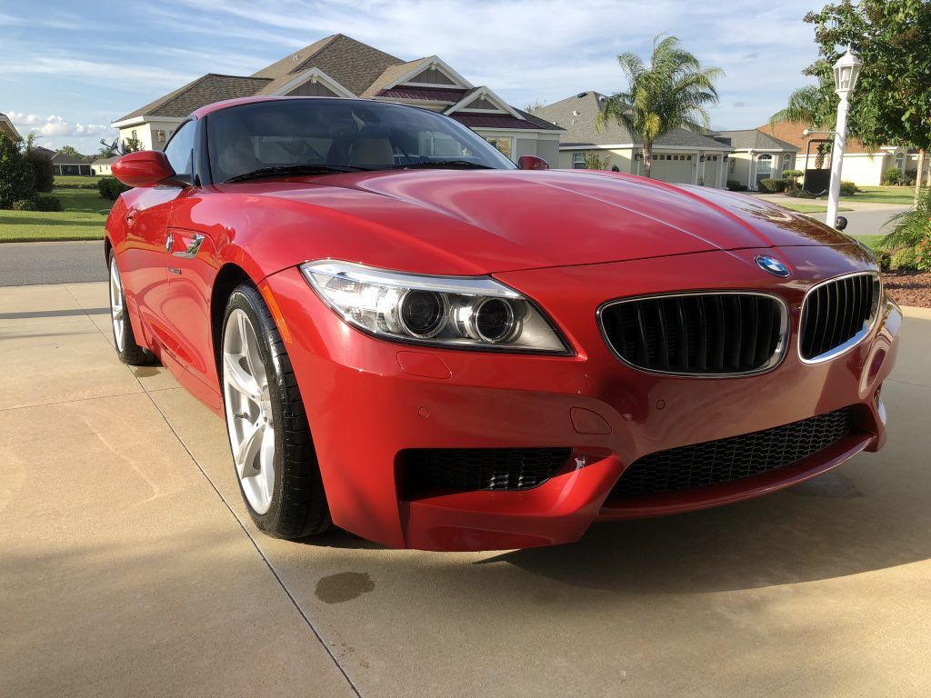 A red bmw z4 is parked in a driveway in front of a house.
