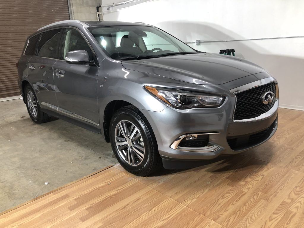 A gray car is parked on a wooden floor in a garage.