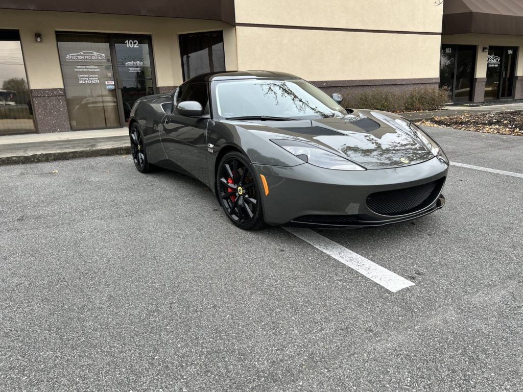 A gray sports car is parked in a parking lot in front of a building.