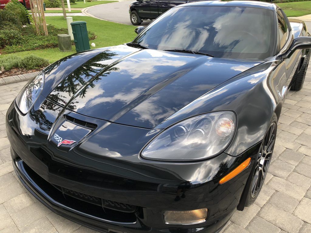 A black corvette is parked on a brick driveway.