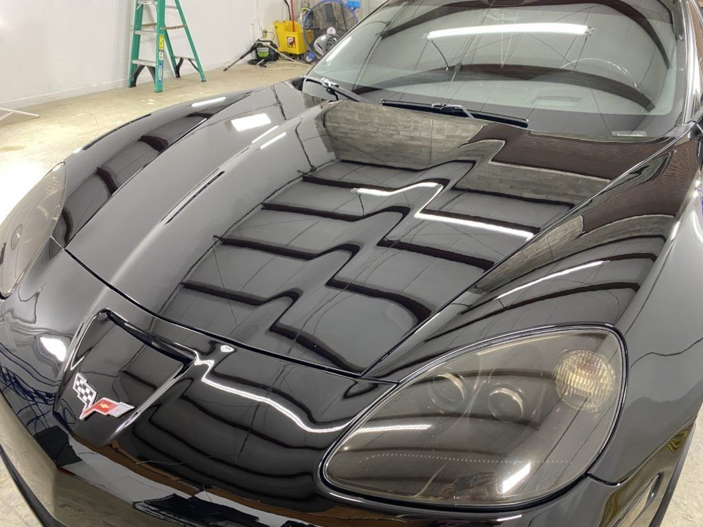 A black sports car is parked in a garage with a ladder in the background.