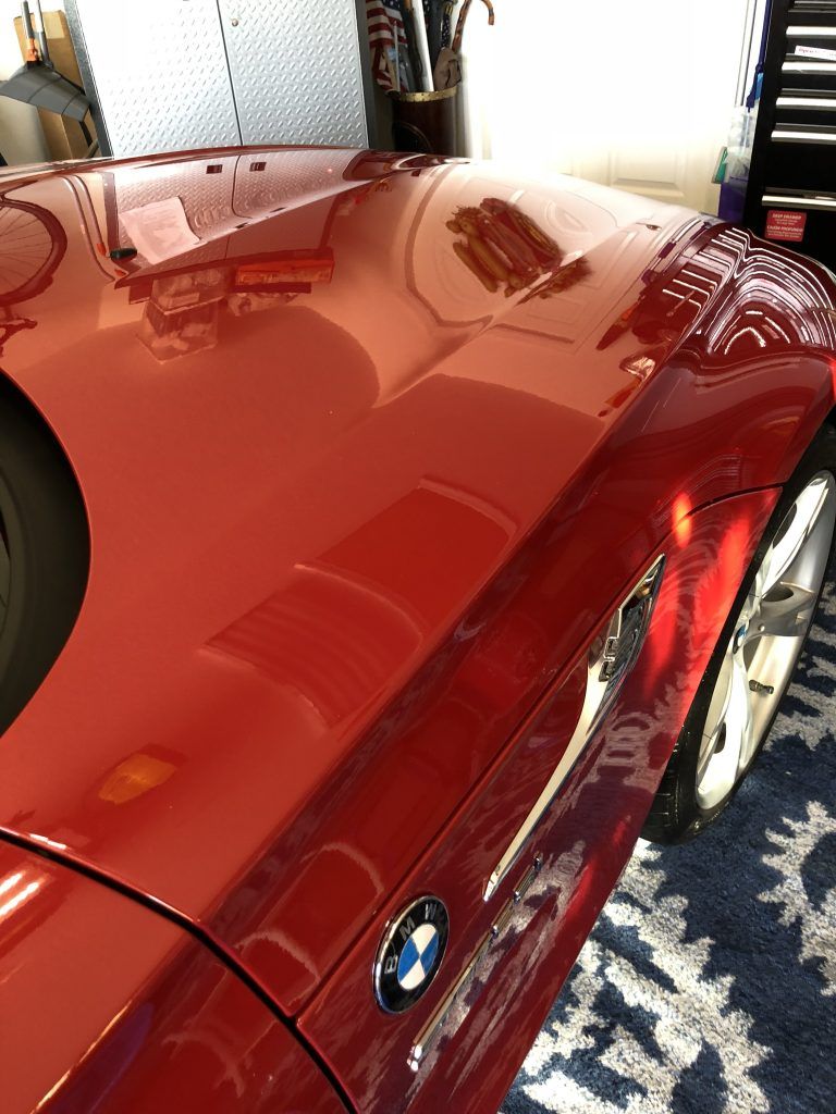 A red bmw is parked in a garage next to a piano.