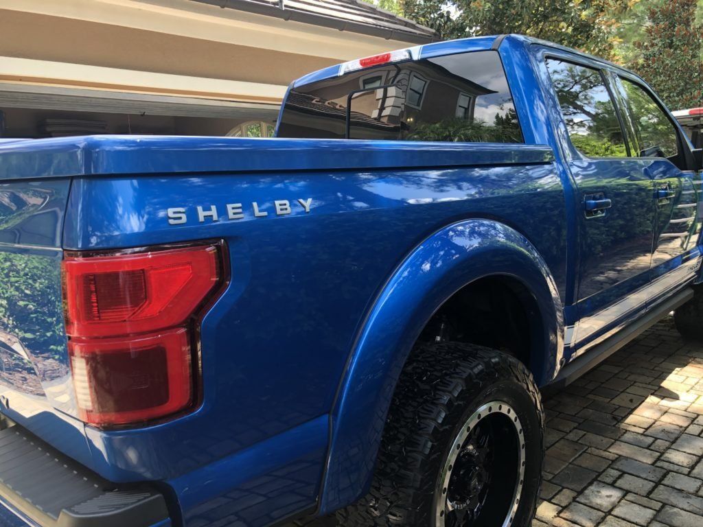 A blue shelby truck is parked in front of a house.