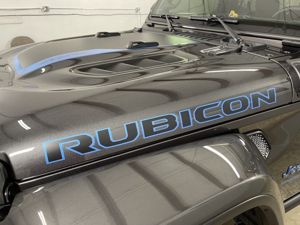 A black jeep with a blue rubicon decal on the hood is parked in a garage.