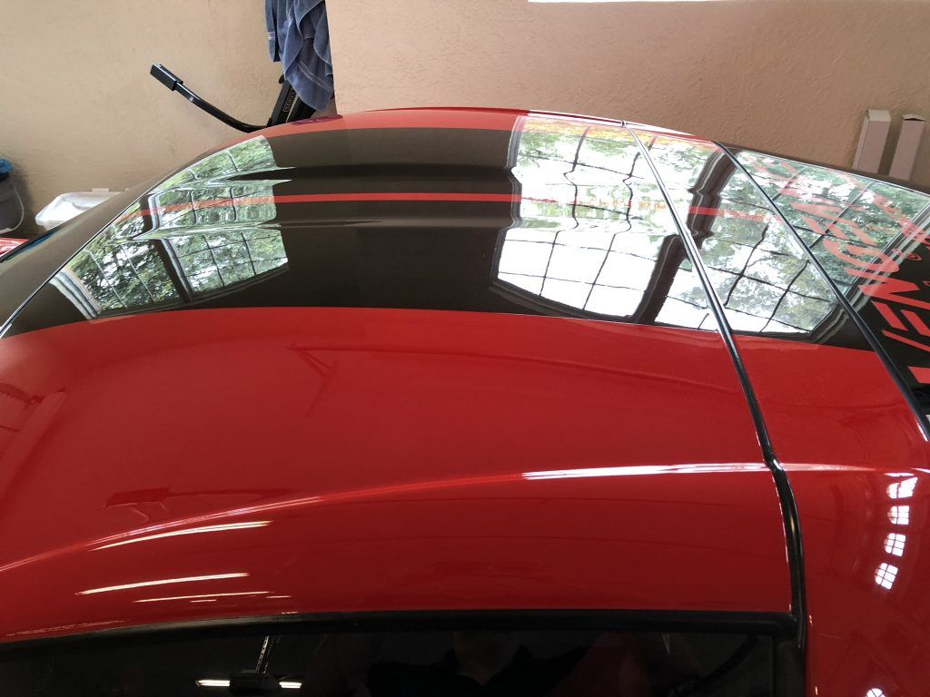 A red car with a black roof is parked in a garage