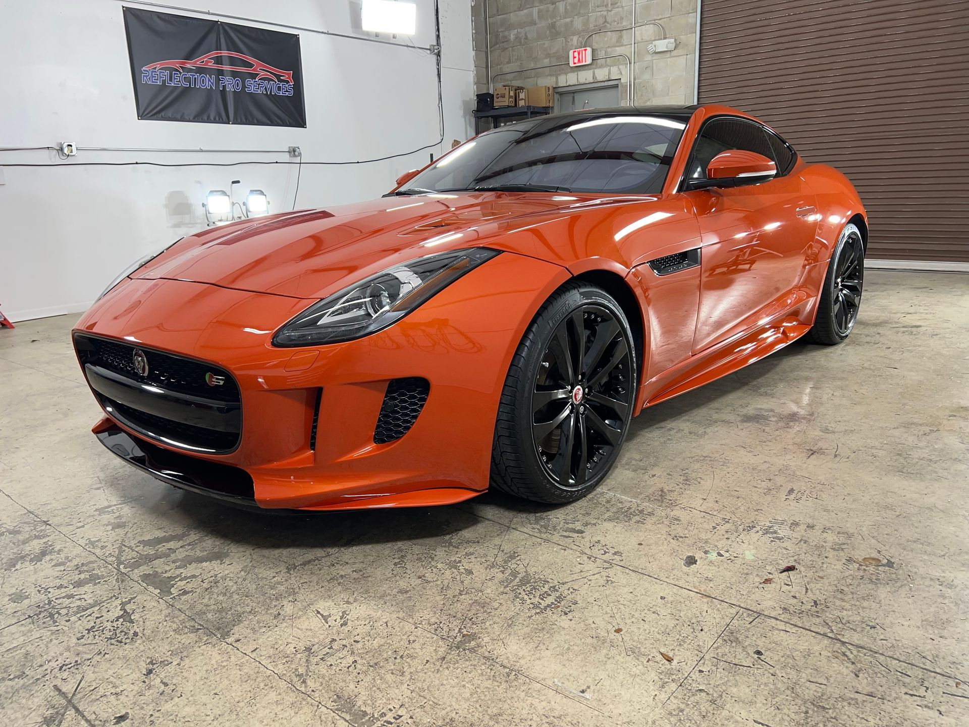 An orange jaguar f type coupe is parked in a garage.