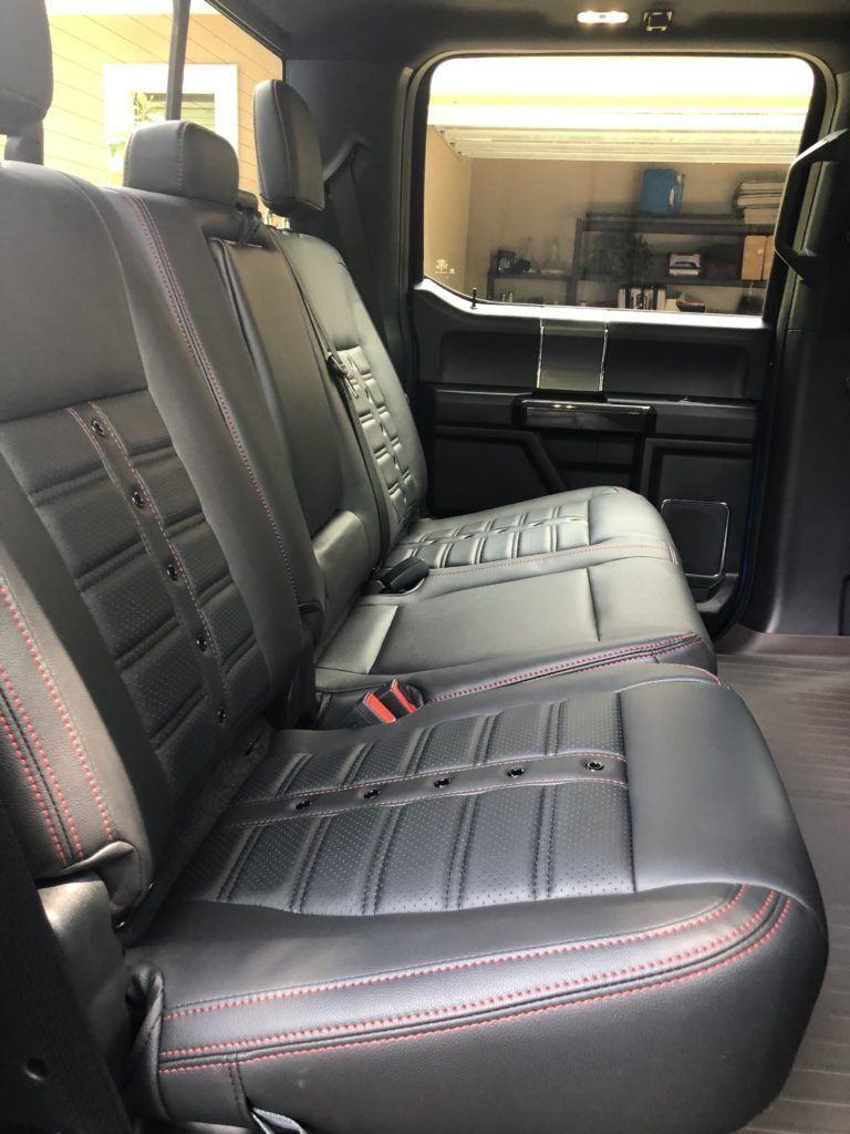 The back seat of a truck with black leather seats and red stitching.