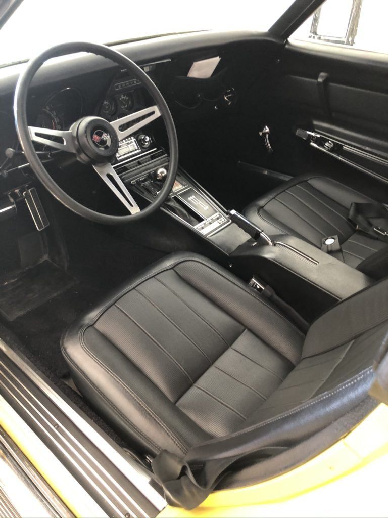 The interior of a yellow corvette with black leather seats and a steering wheel.
