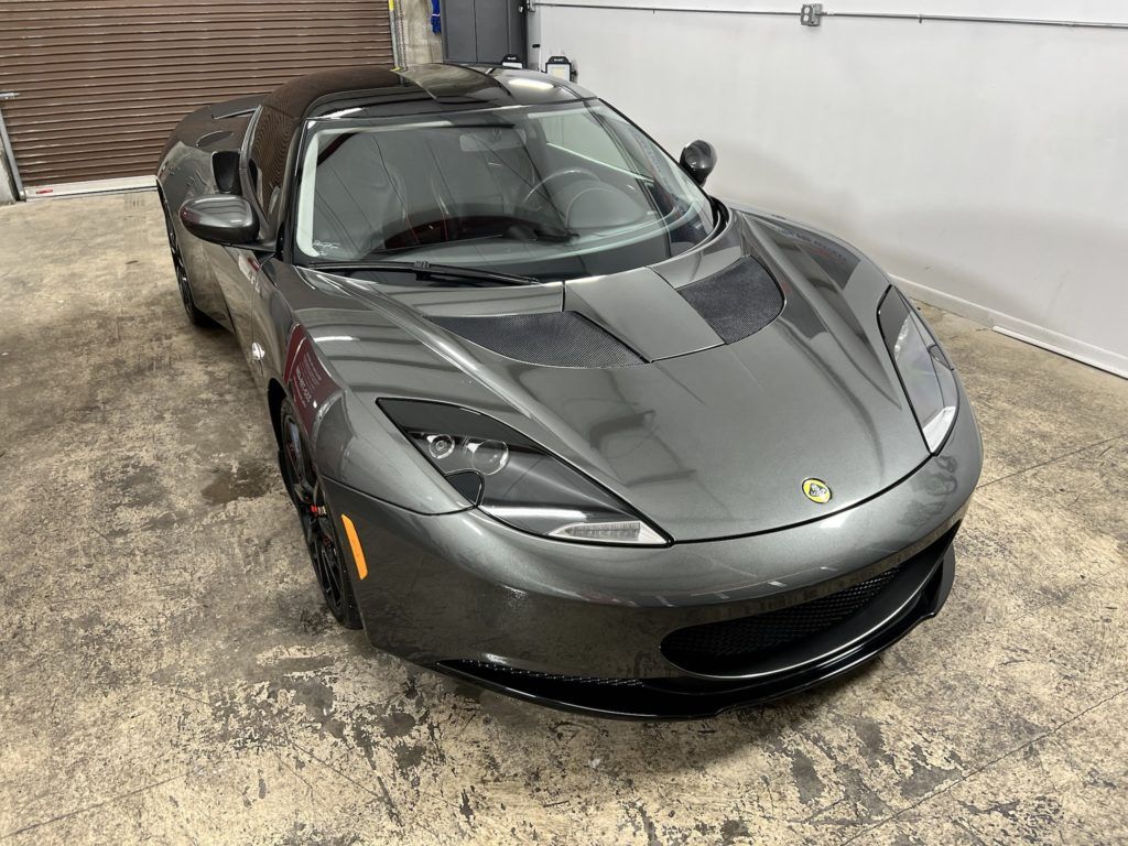 A gray sports car is parked in a garage next to a garage door.