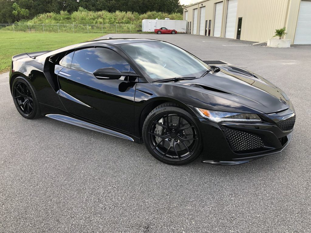 A black sports car is parked in a parking lot in front of a building.