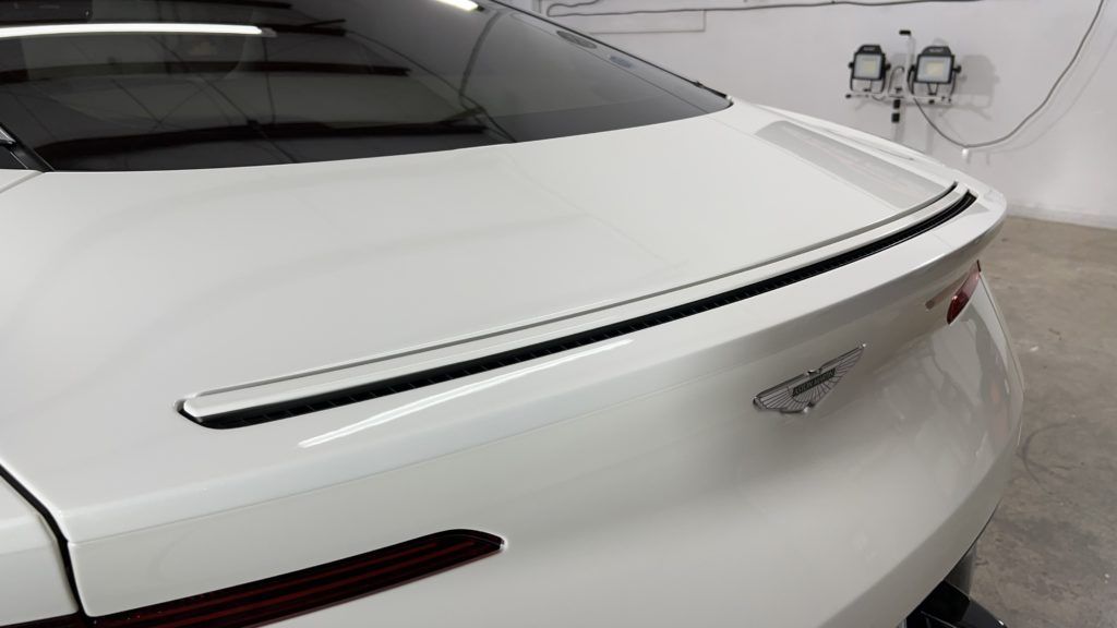 A white car with a black spoiler is parked in a garage.