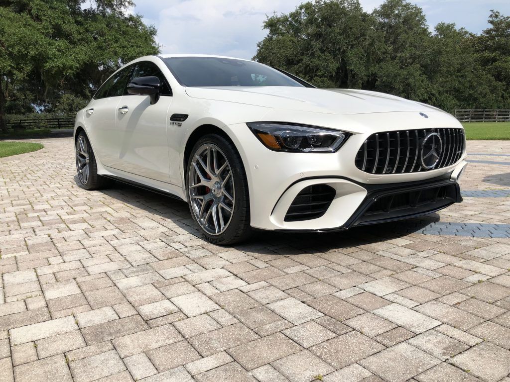 A white mercedes amg gt 63 s is parked on a brick driveway.