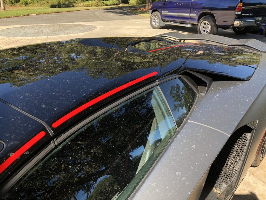A black car with red stripes on the roof is parked next to a blue truck.