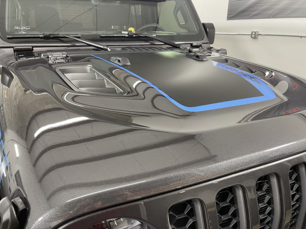 A black jeep with a blue stripe on the hood is parked in a garage.