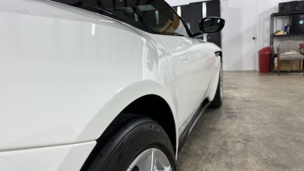 A white car is parked in a garage with a black tire.
