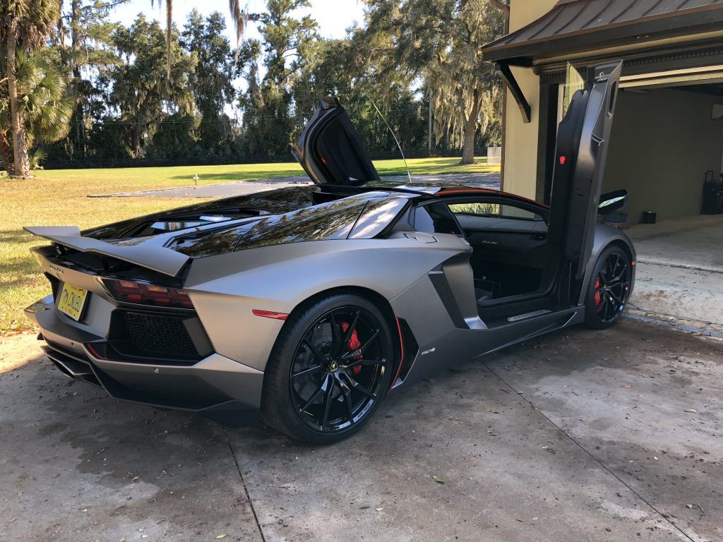 A black lamborghini aventador is parked in front of a garage with its doors open.