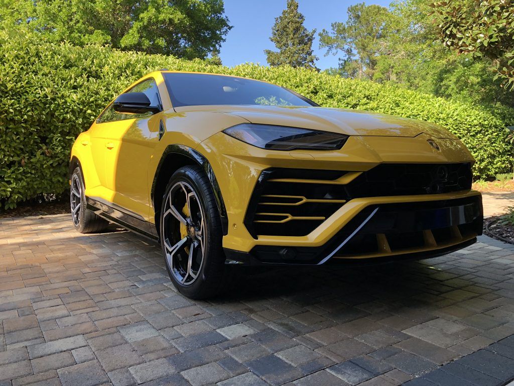 A yellow lamborghini urus is parked on a brick driveway.