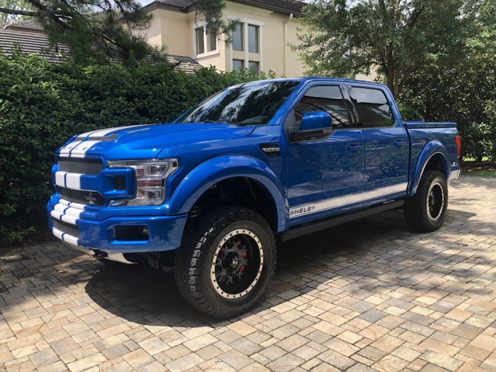 A blue ford f150 is parked on a brick driveway in front of a house.