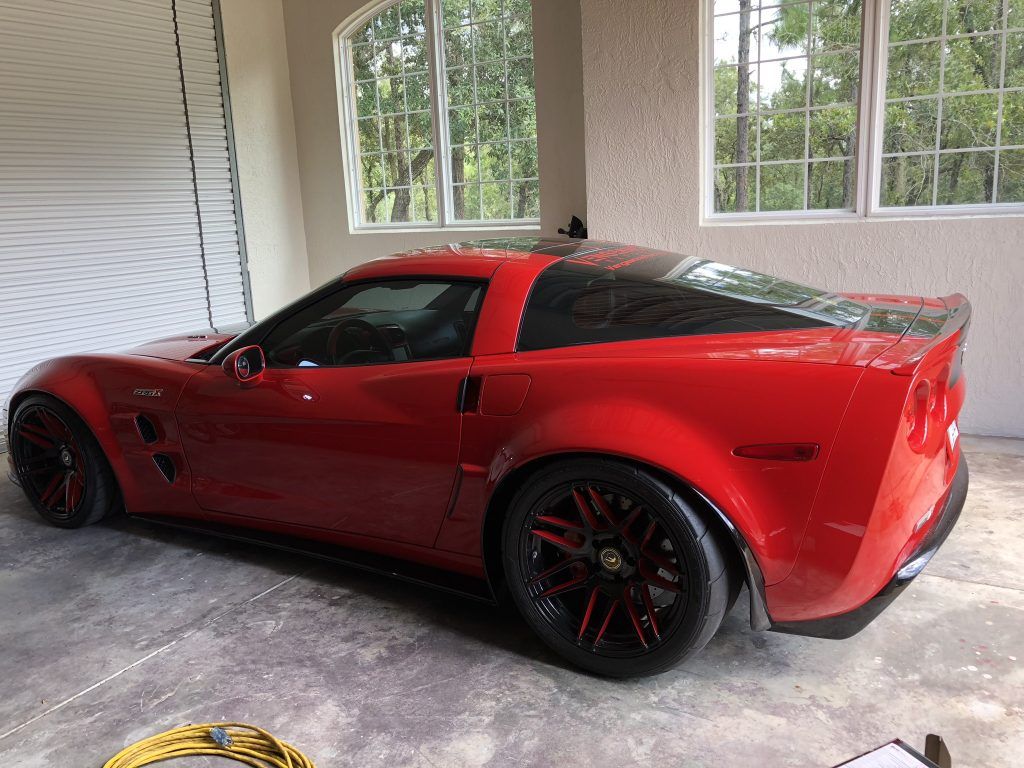 A red sports car is parked in a garage next to a window.