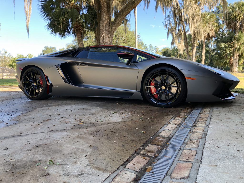 A lamborghini aventador is parked in a driveway next to a tree.
