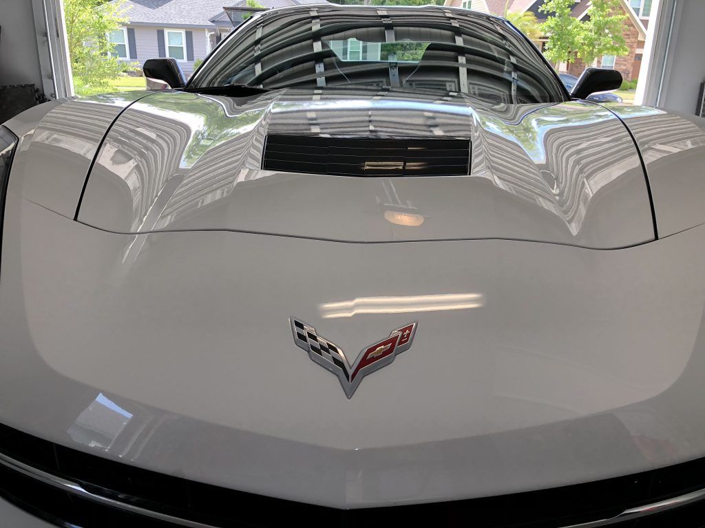 A white corvette is parked in a garage with the hood up.