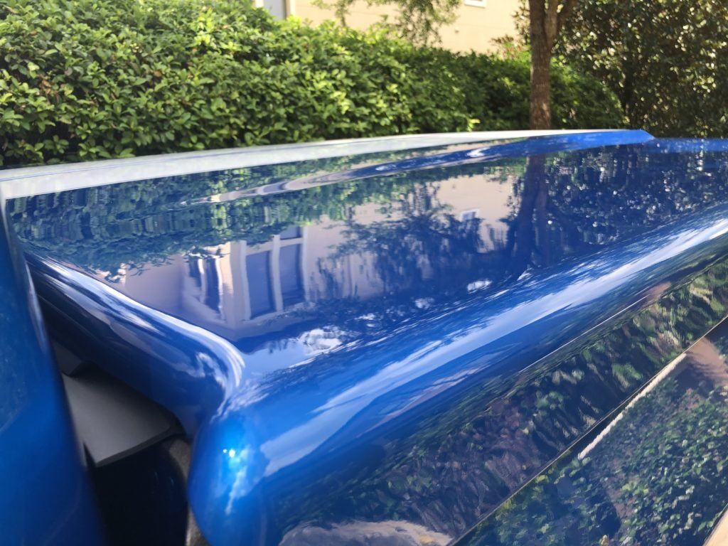 A blue car is parked in front of a hedge.