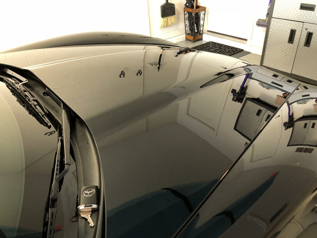 A black car is parked in a garage with the hood up.