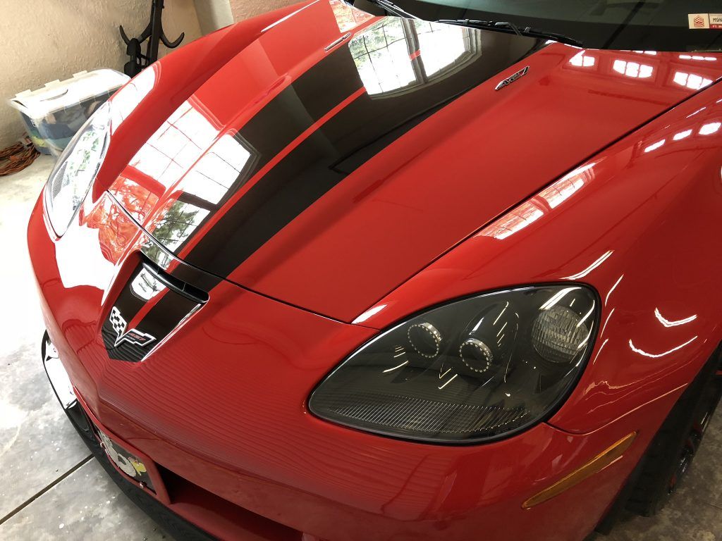 A red corvette with black stripes on the hood