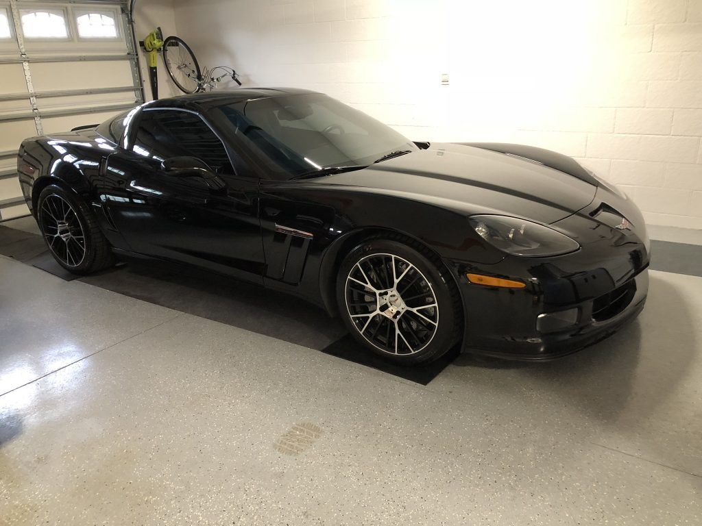 A black sports car is parked in a garage next to a bicycle.