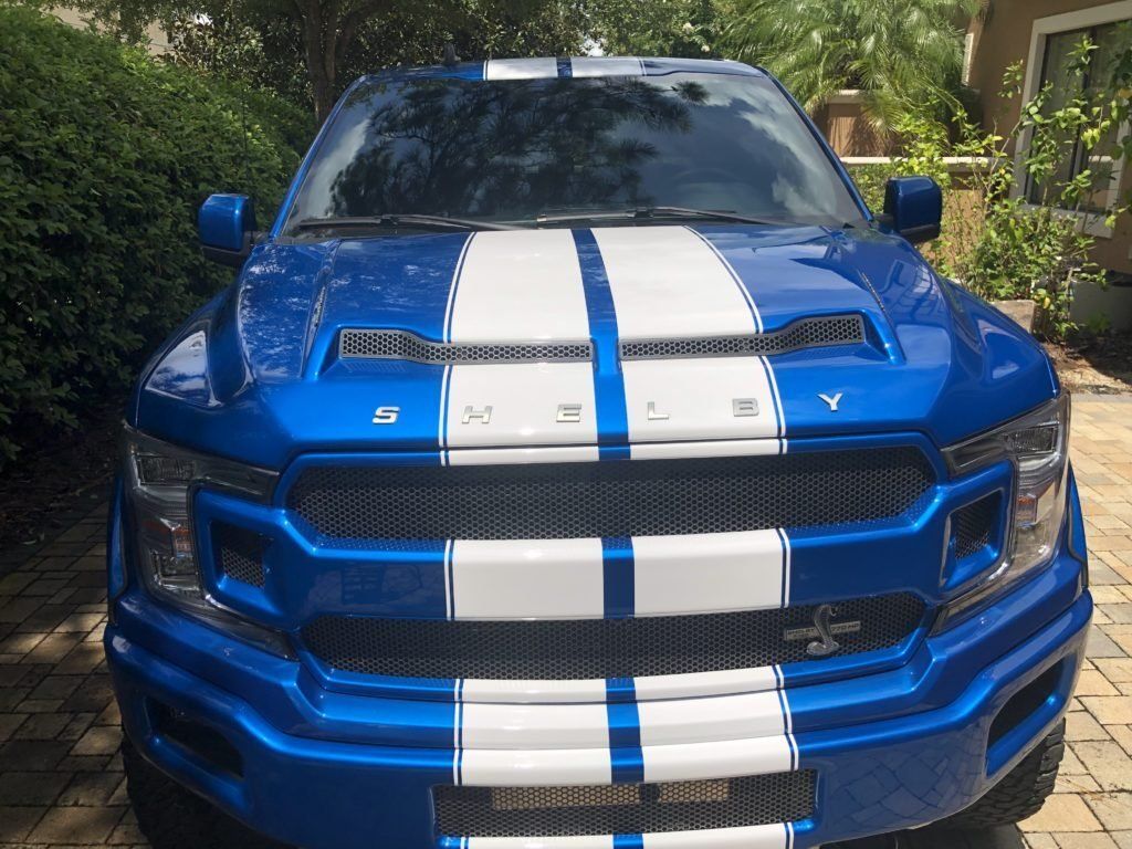 A blue truck with white stripes on the front is parked in a driveway.