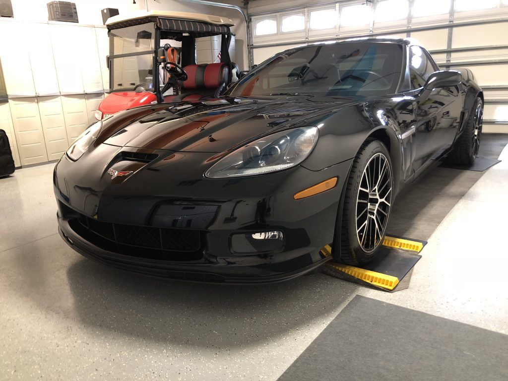 A black corvette is parked in a garage next to a golf cart.