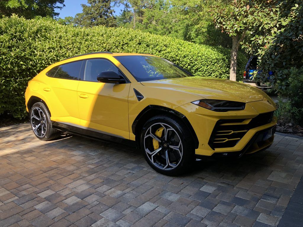 A yellow lamborghini urus is parked on a brick driveway.