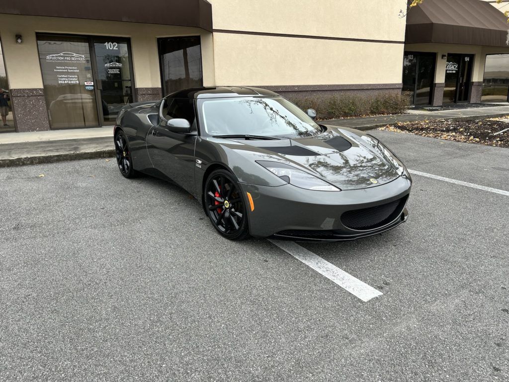 A gray sports car is parked in a parking lot in front of a building.