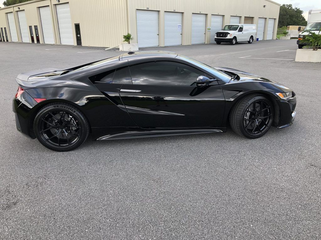 A black sports car is parked in a parking lot in front of a building.