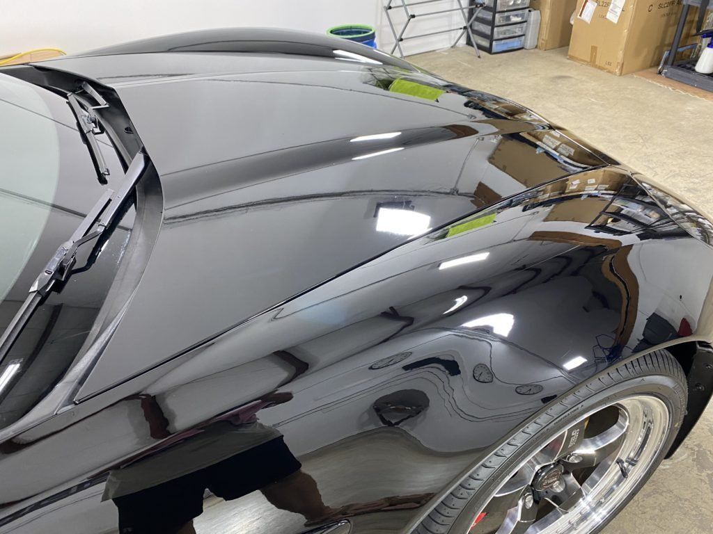 A black car is parked in a garage with the hood up.