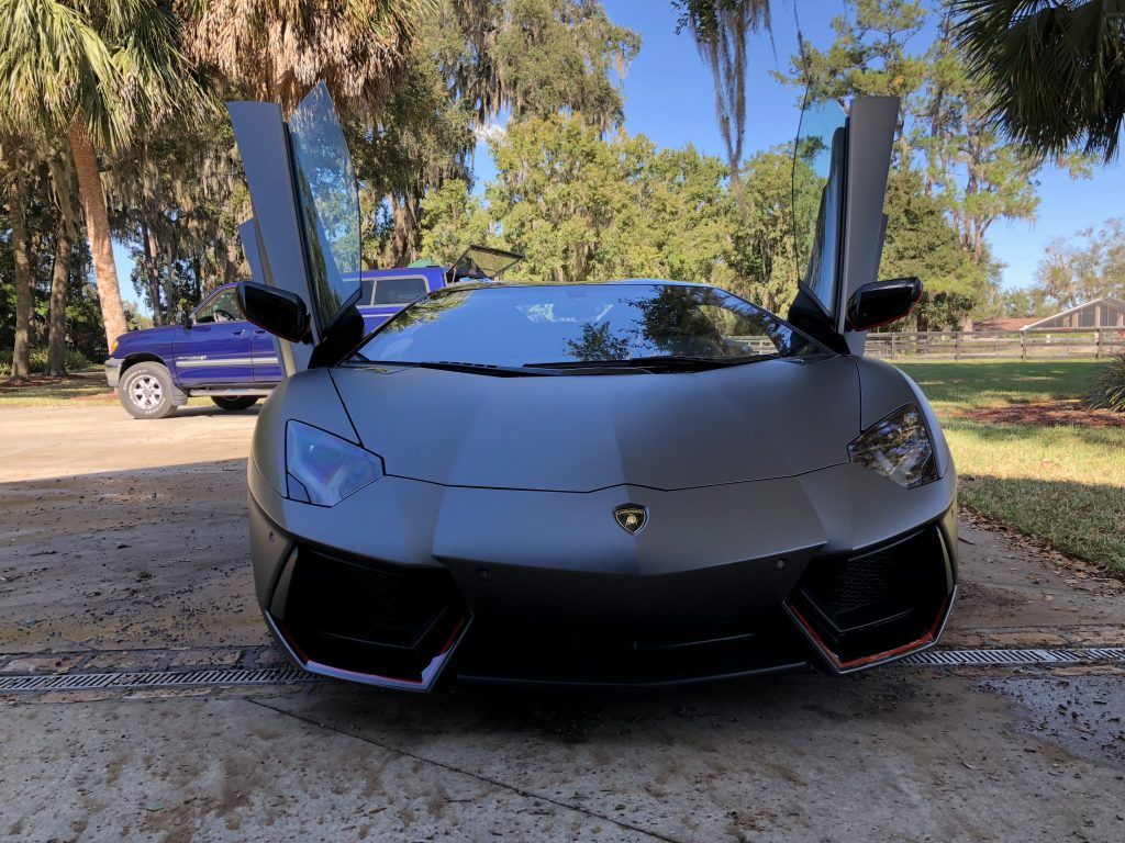 A black lamborghini aventador is parked in a driveway with its doors open.