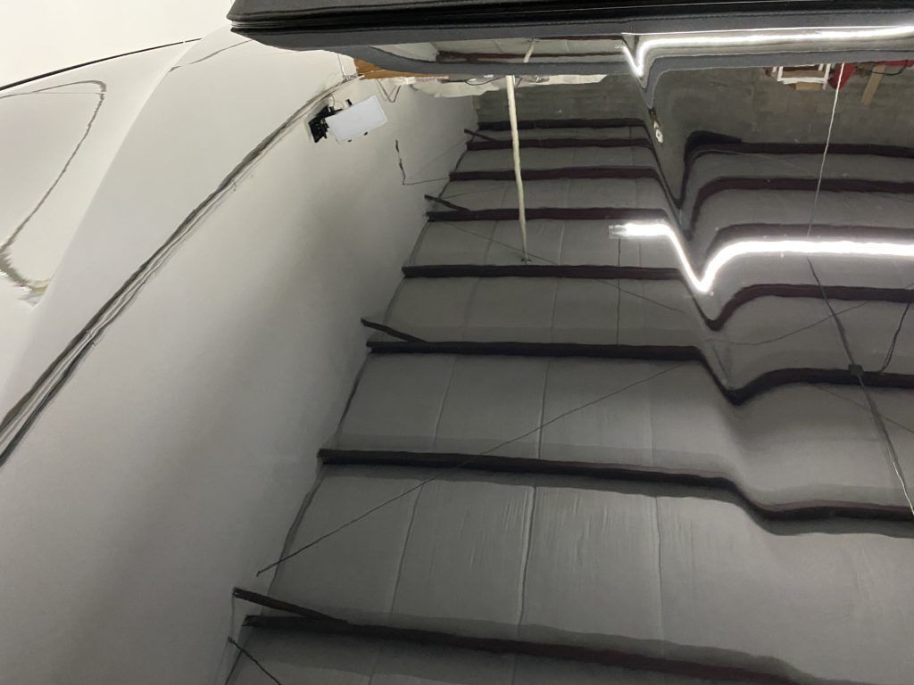 A car is parked in a garage with stairs leading up to it.