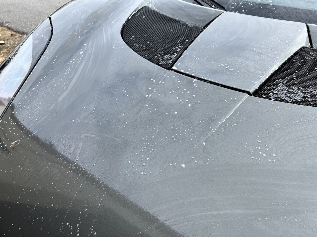 A close up of the hood of a car with water drops on it.