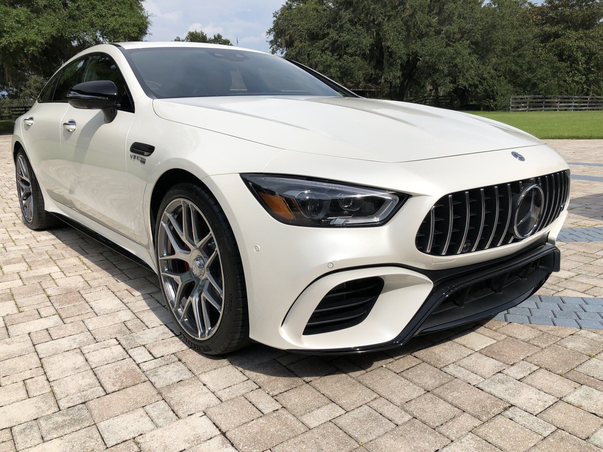 A white mercedes amg gt 63 s is parked on a brick driveway.