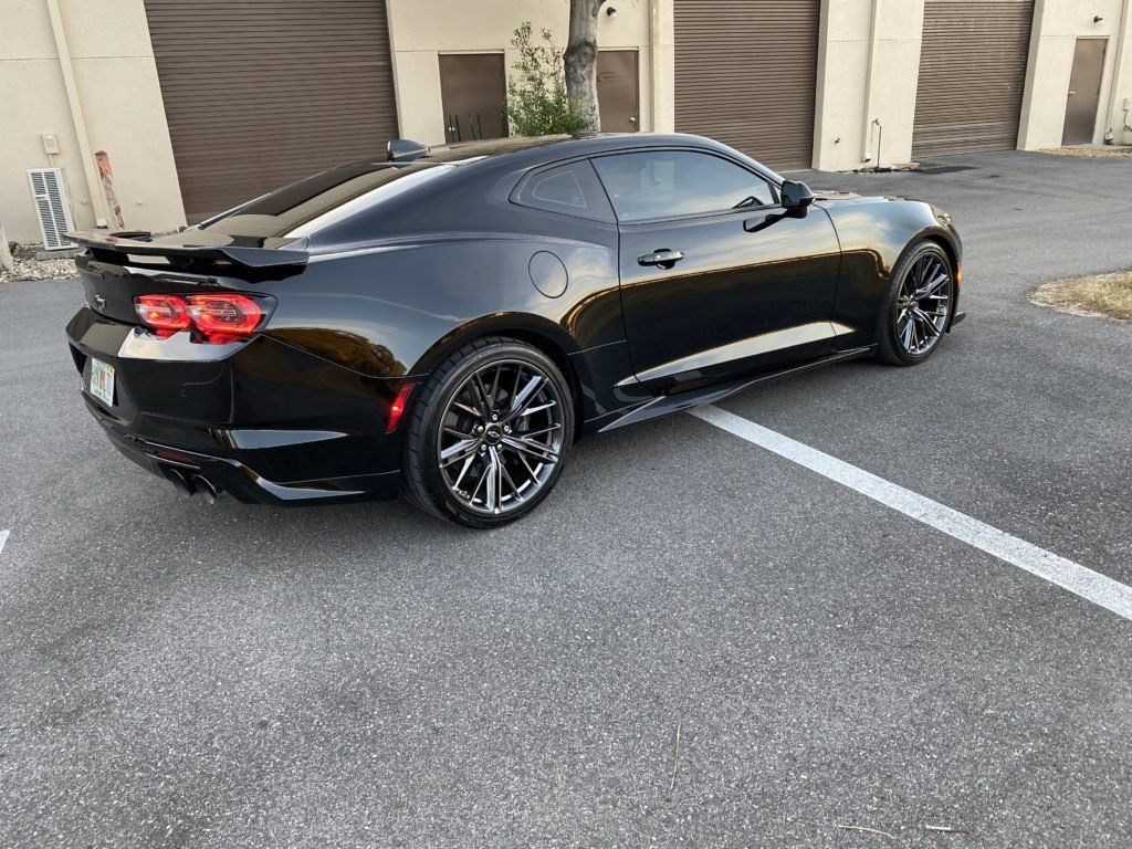 A black car is parked in a parking lot in front of a garage.