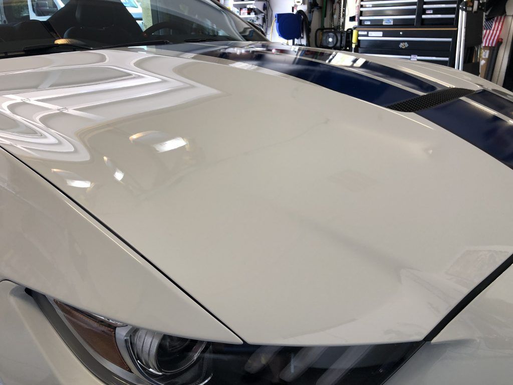 A close up of a white car with a blue stripe on the hood.
