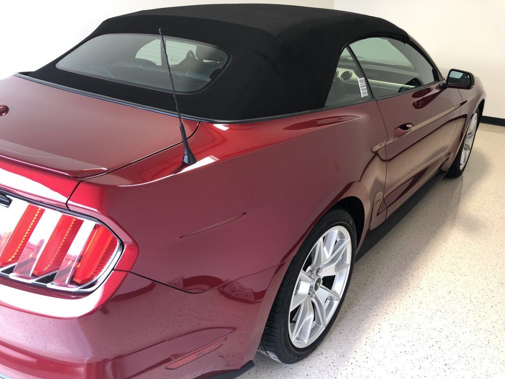 A red convertible mustang with a black top is parked in a garage.