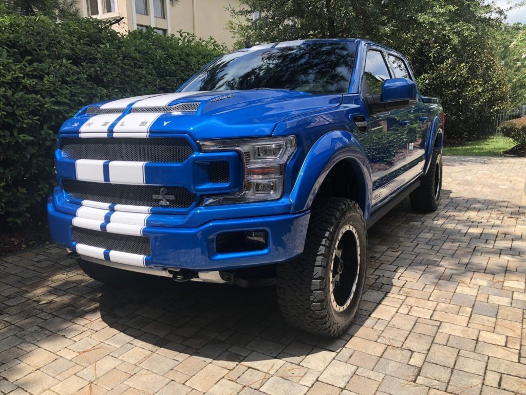 A blue ford f150 is parked on a brick driveway.
