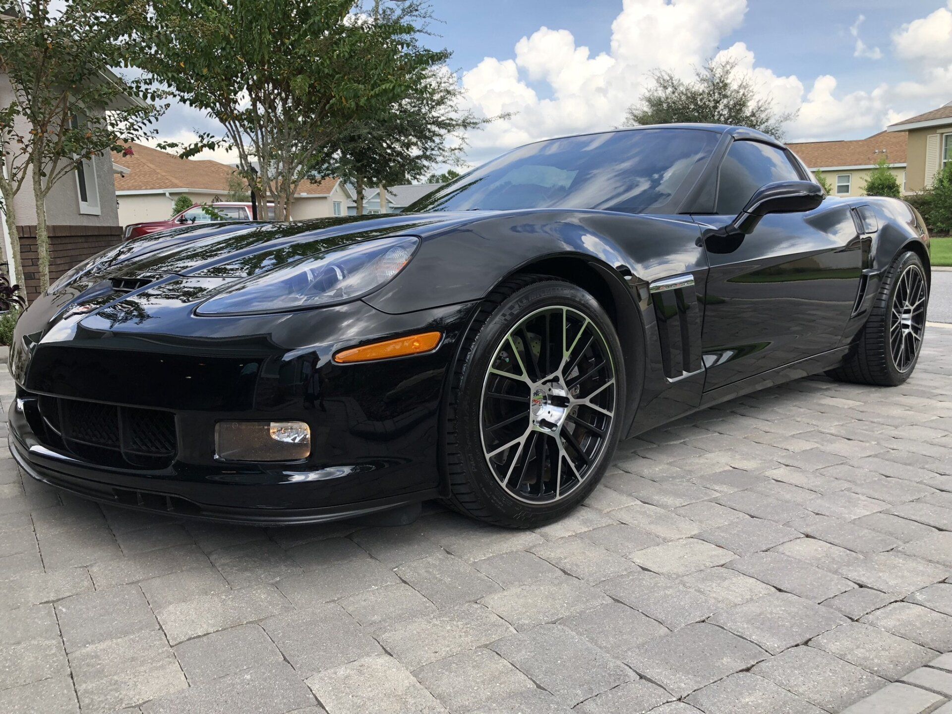 A black corvette is parked on a brick driveway in front of a house.
