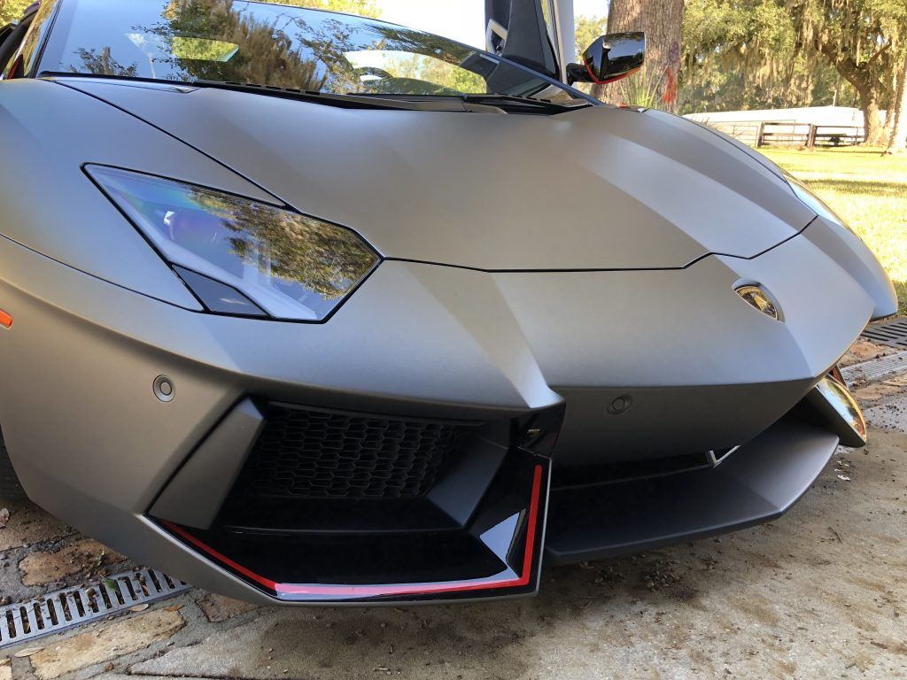 A black lamborghini aventador is parked in the dirt.